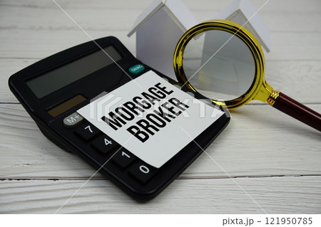 Mortgage Broker text message on sticky note with alarm clock, magnifying glass and calculator on wooden background 121950785