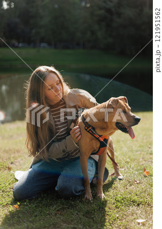 young woman walks with her dog in the park. A lady in a beige raincoat is playing with a pit bull 121951562