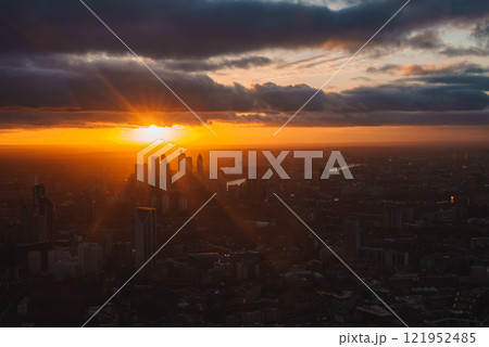 The image shows a sunset over London, highlighting skyscrapers and the River Thames. The sky is vibrant with dramatic clouds, reflecting the setting sun. The image shows a sunset over London, highlighting skyscrapers and the River Thames. The sky is vibrant with dramatic clouds, reflecting the setting sun. 121952485