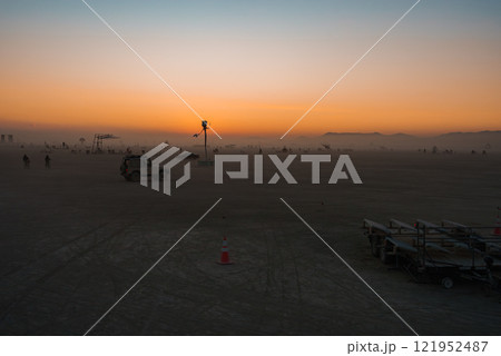A vast desert scene at sunset in Black Rock Desert, Nevada, features art installations, vehicles, and participants. Distant mountains frame the horizon. A vast desert scene at sunset in Black Rock Desert, Nevada, features art installations, vehicles, and participants. Distant mountains frame the horizon. 121952487