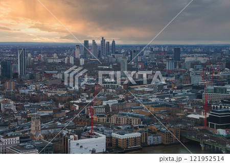 London's skyline features historic and modern architecture, with skyscrapers and the River Thames. A warm sunset glow highlights construction cranes. 121952514