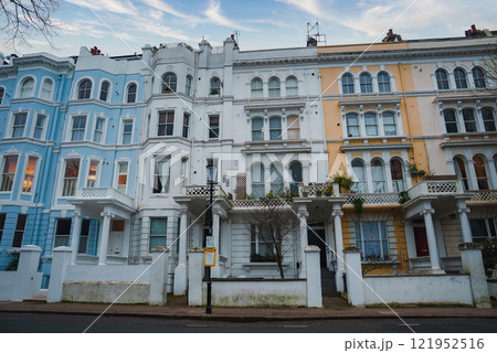 A row of colorful Victorian terraced houses in London features ornate details, pastel hues, large bay windows, and decorative balconies under a clear winter sky. 121952516