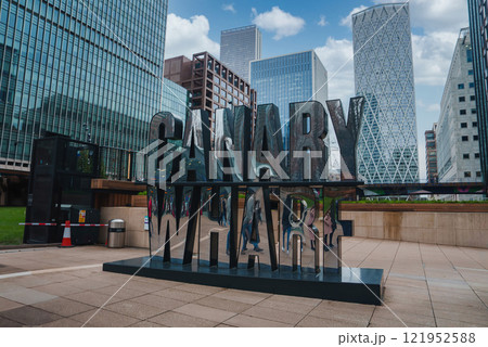 The iconic Canary Wharf sign is set against modern skyscrapers, including One Canada Square, under a clear blue sky in London's financial district. The iconic Canary Wharf sign is set against modern skyscrapers, including One Canada Square, under a clear blue sky in London's financial district. 121952588