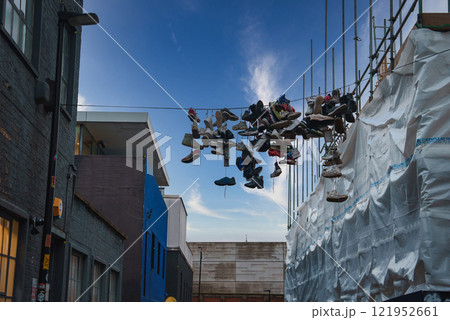A collection of shoes hangs from a wire between modern and older buildings in London, with scaffolding and clear skies adding to the urban atmosphere. A collection of shoes hangs from a wire between modern and older buildings in London, with scaffolding and clear skies adding to the urban atmosphere. 121952661