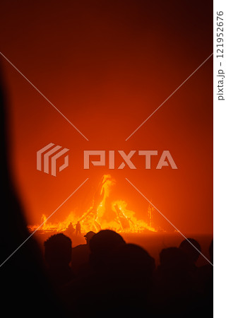 Silhouettes of people watch a large fire against a dark night sky, with intense orange and red flames at the Burning Man festival in Black Rock Desert. 121952676