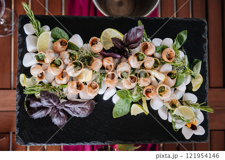 Gourmet escargot platter with fresh herbs and lemon, elegantly presented on a slate serving board 121954146