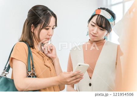 アパレルショップで買い物中にスマホを見ながら悩む女性客 アパレルショップで買い物中にスマホを見ながら悩む女性客 121954506