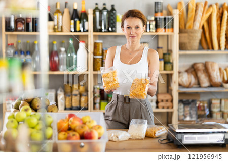 Adult woman seller offering corn flakes in grocery Adult woman seller offering corn flakes in grocery 121956945