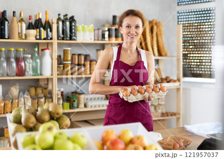 Female seller selling food products offers to buy chicken eggs in supermarket 121957037