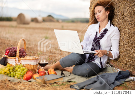 Businesswoman working on laptop during picnic near haystack Businesswoman working on laptop during picnic near haystack 121957042
