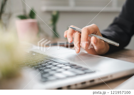 Close-up of Hand Using Pen on Laptop Touchpad in Modern Office Setting with Greenery in Background Close-up of Hand Using Pen on Laptop Touchpad in Modern Office Setting with Greenery in Background 121957100