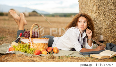 Relaxed businesswoman lying near haystack with wine and book 121957207