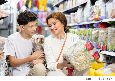 Woman with teenage son and Yorkshire terrier choosing hay for rabbit cage in store Woman with teenage son and Yorkshire terrier choosing hay for rabbit cage in store 121957357