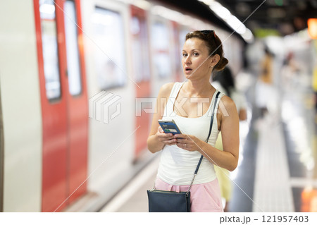 Portrait of gorgeous woman waiting for subway train with smartphone in hands at underground station 121957403