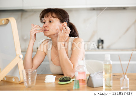 Woman checking facial skin condition in mirror at home 121957437