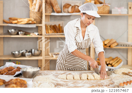 Skilled female baker slicing dough in artisan bakery 121957467