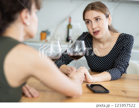 Sad woman sits silently in kitchen, friend sympathize and comfort her Sad woman sits silently in kitchen, friend sympathize and comfort her 121957522
