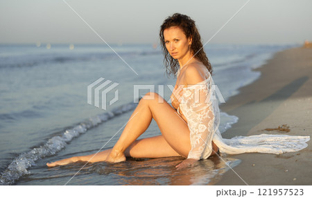 Adult woman in white peignoir sitting on coast 121957523