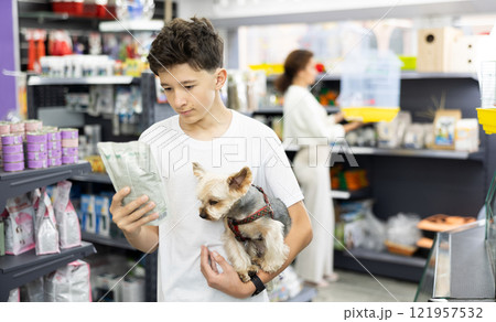 Boy with dog Yorkshire terrier in arms and read composition of product at packaging of dog dry food Boy with dog Yorkshire terrier in arms and read composition of product at packaging of dog dry food 121957532