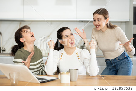 Three happy middle-aged woman expressing joy for winning in the kitchen Three happy middle-aged woman expressing joy for winning in the kitchen 121957538