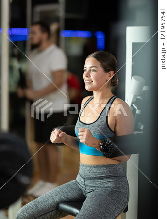 Girl in gym performs exercises for arm muscles using simulators and fitness center equipment. Girl in gym performs exercises for arm muscles using simulators and fitness center equipment. 121957541