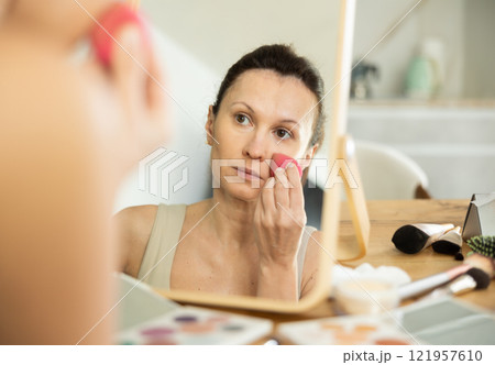 Woman applying foundation with makeup sponge in front of mirror 121957610