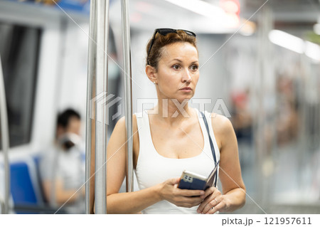 Adult woman standing in subway car with phone Adult woman standing in subway car with phone 121957611
