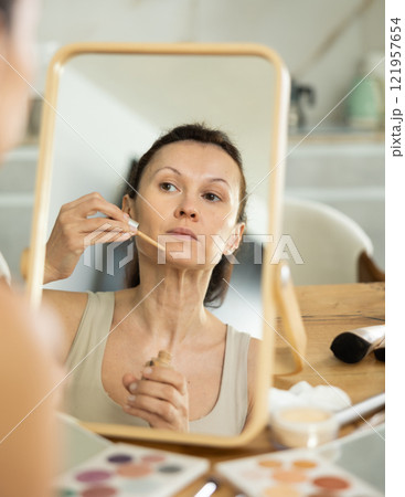 Middle-aged woman applying liquid foundation on her face Middle-aged woman applying liquid foundation on her face 121957654