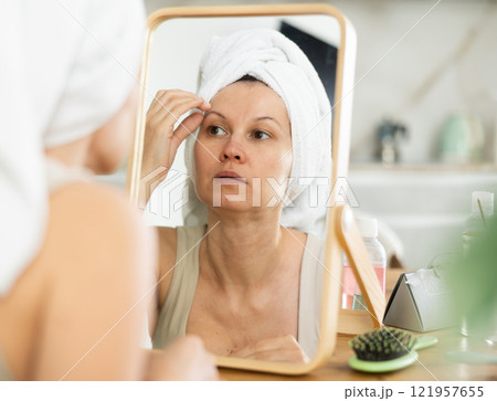 Middle-aged woman examining her facial skin looking in the mirror put on the table Middle-aged woman examining her facial skin looking in the mirror put on the table 121957655