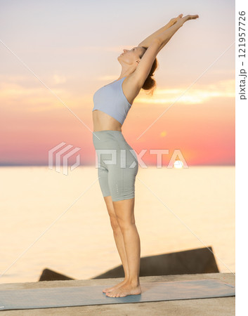 Near sea during sunset, girl performs Tiryaka Tadasana 121957726