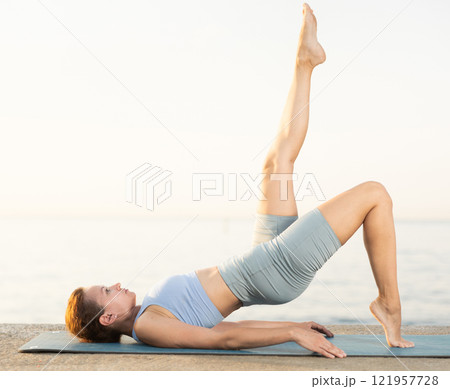Near sea during sunset, girl performs Setu Badha Sarvangasana Near sea during sunset, girl performs Setu Badha Sarvangasana 121957728