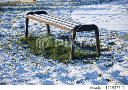 Wooden Bench in a Snowy Park with Frost-Covered Grass Wooden Bench in a Snowy Park with Frost-Covered Grass 121957741
