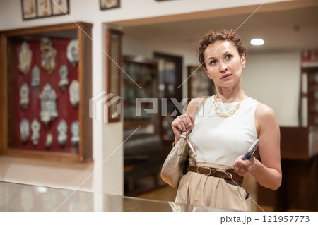 Woman with piece of paper and phone in hands walks around museum hall, view exhibition 121957773