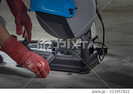Worker cutting steel rectangular pipe in construction site. 121957822