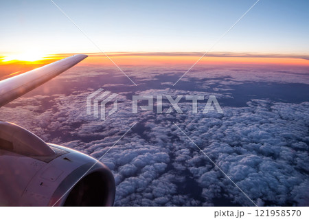 Wing view of aircraft flying above the clouds in the sky at the sunset Wing view of aircraft flying above the clouds in the sky at the sunset 121958570