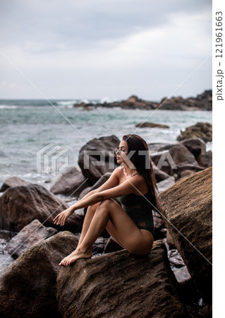 Serene Seaside Retreat A woman enjoying her time on a beautiful rocky shoreline by the ocean Serene Seaside Retreat A woman enjoying her time on a beautiful rocky shoreline by the ocean 121961663
