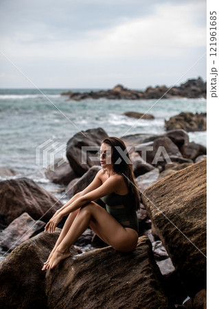 Serene Seaside Retreat A woman enjoying her time on a beautiful rocky shoreline by the ocean Serene Seaside Retreat A woman enjoying her time on a beautiful rocky shoreline by the ocean 121961685
