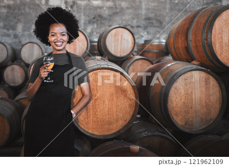Portrait of a young woman winemaker standing with a glass with wooden barrel of red wine in a winery cellar or distillery. Entrepreneur or business owner working for startup success business success 121962109