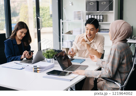 Happy businesspeople while collaborating on a new project in an office. Group of diverse businesspeople using a laptop and tablet 121964002