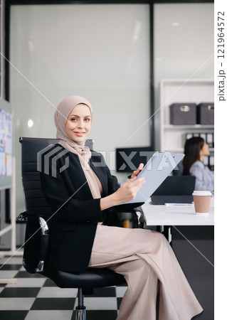 Young Arabic female entrepreneur wearing a hijab working online with a laptop at modern office 121964572