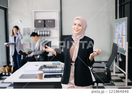 Confident female entrepreneur looking at the camera while standing. Young businesswoman standing in the boardroom Confident female entrepreneur looking at the camera while standing. Young businesswoman standing in the boardroom 121964848