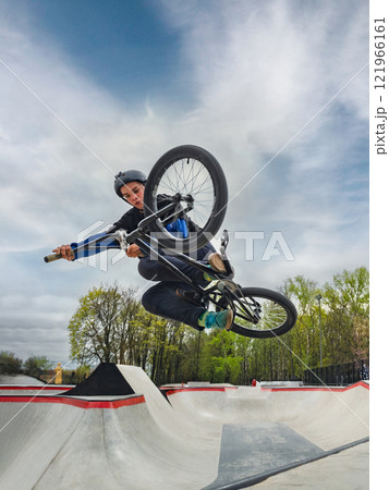 BMX bicycle rider doing stunt Tabletop. Skilled BMX freestyler athlete jumping and doing aerial trick Table top in street ramp park outdoors. Amazing blue sky 121966161