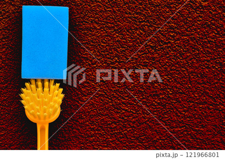 Orange brush blue sponge for cleaning on red plastered surface Orange brush blue sponge for cleaning on red plastered surface 121966801