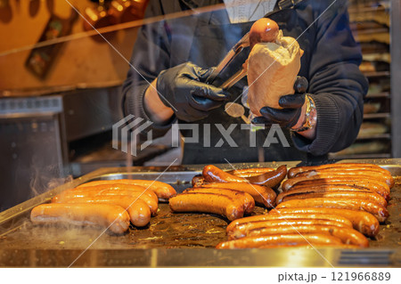 Grilled sausages being prepared on food stand with hands in gloves holding bread roll. Concept of street food 121966889