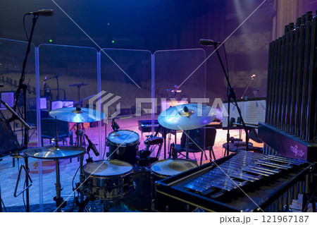 Drum kit, bells and metallophone with microphone support behind a transparent noise-absorbing barrier 121967187