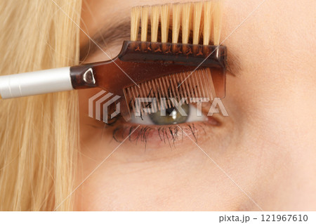 Woman brushing her eyelashes Woman brushing her eyelashes 121967610