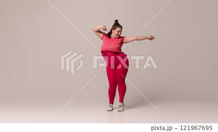 Smiling chubby woman dressed sportswear gracefully leaning with extended arm against white studio background. Fashion and style. Smiling chubby woman dressed sportswear gracefully leaning with extended arm against white studio background. Fashion and style. 121967695