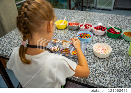 Little girl learning how to cook in a cooking class. Handmade dessert. Making chocolate candy, Child filling heart shaped mold with chocolate Little girl learning how to cook in a cooking class. Handmade dessert. Making chocolate candy, Child filling heart shaped mold with chocolate 121968481