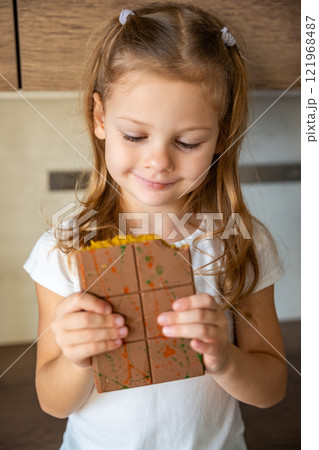 Dubai chocolate with pistachio paste and kataifi dough in hands of little girl. Confectionery handmade sweets at home in the kitchen. Dubai chocolate with pistachio paste and kataifi dough in hands of little girl. Confectionery handmade sweets at home in the kitchen. 121968487