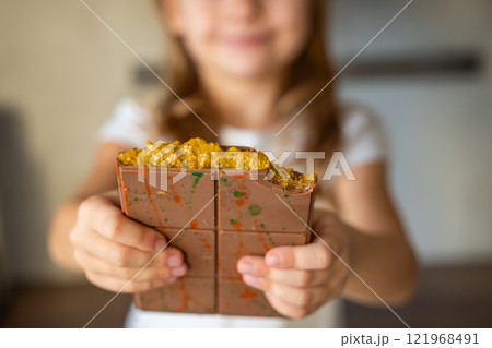 Dubai chocolate with pistachio paste and kataifi dough in hands of little girl. Confectionery handmade sweets at home in the kitchen.  121968491